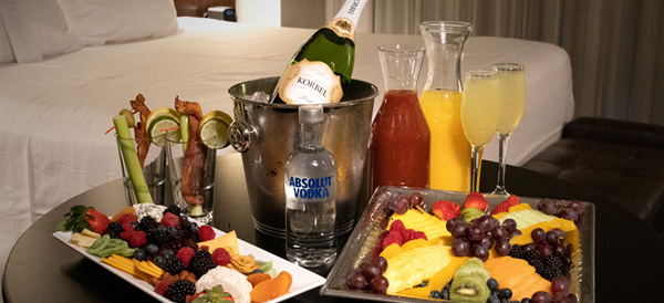 Room coffee table with bottle of champagne on ice, bottle of Absolut vodka, mimosas, bloody marys, fruit platters, and cocktail skewers